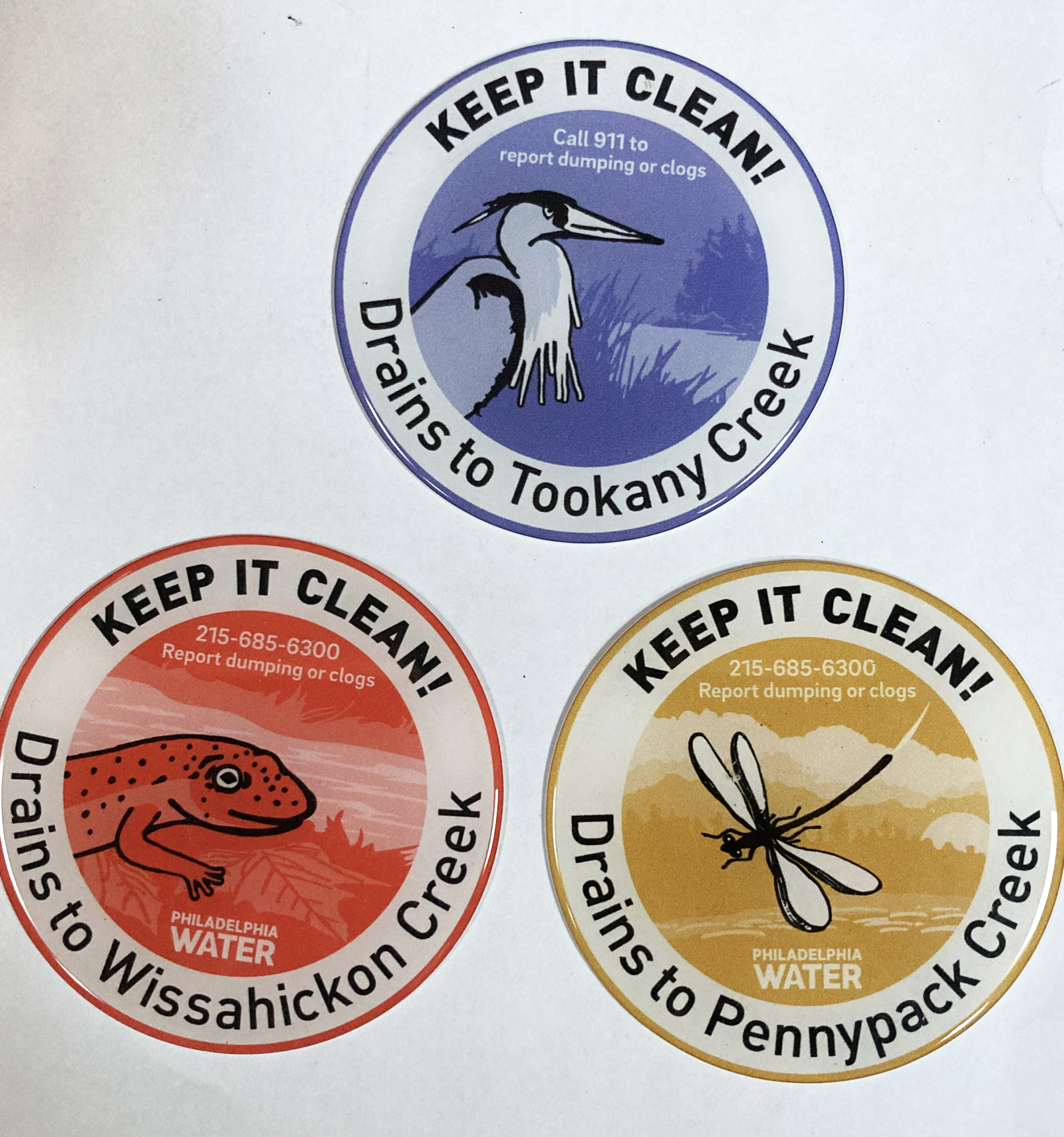 Storm drain markers that say "Keep it Clean, Call 911 to report dumping or clogs"