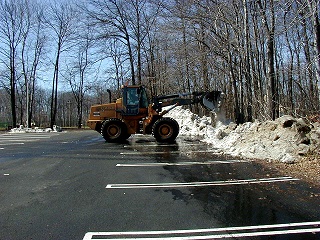 A snow plow plowing snow from a parking lot. 