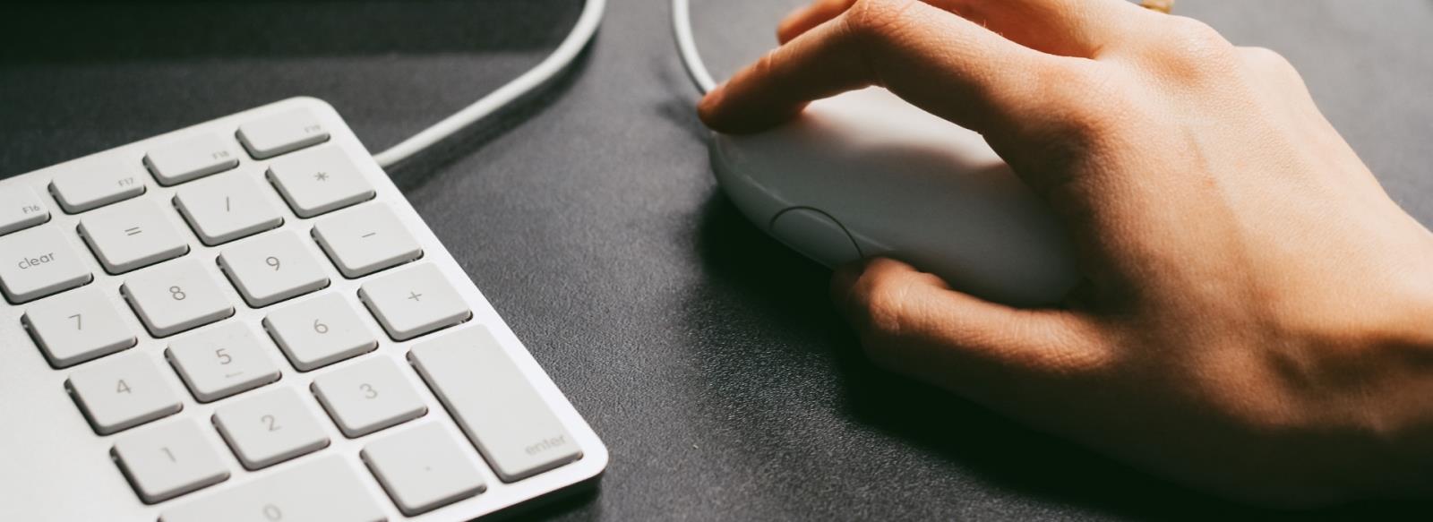 Image of hand clicking computer mouse and keyboard.