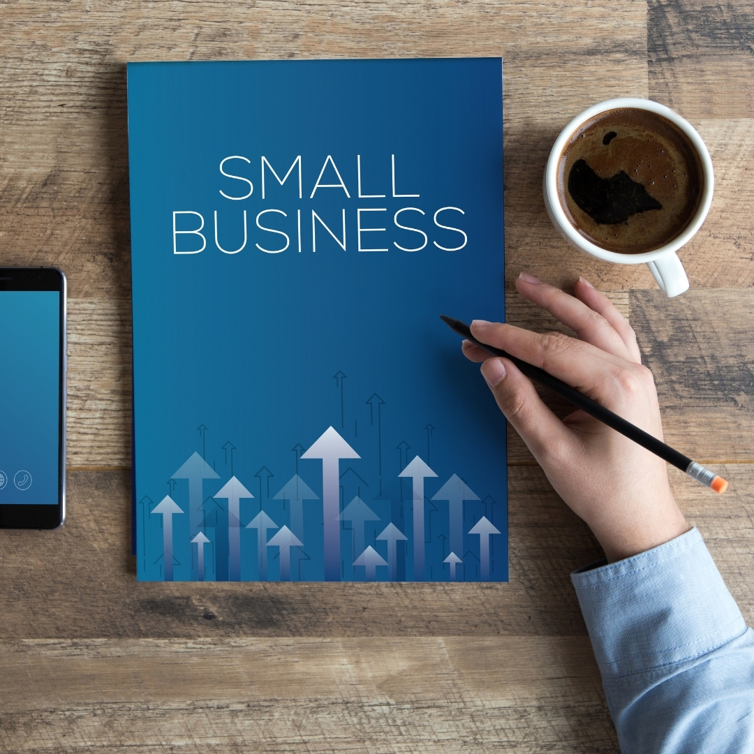 image with a hand holding a pen, coffee cup, and notebook that says small business