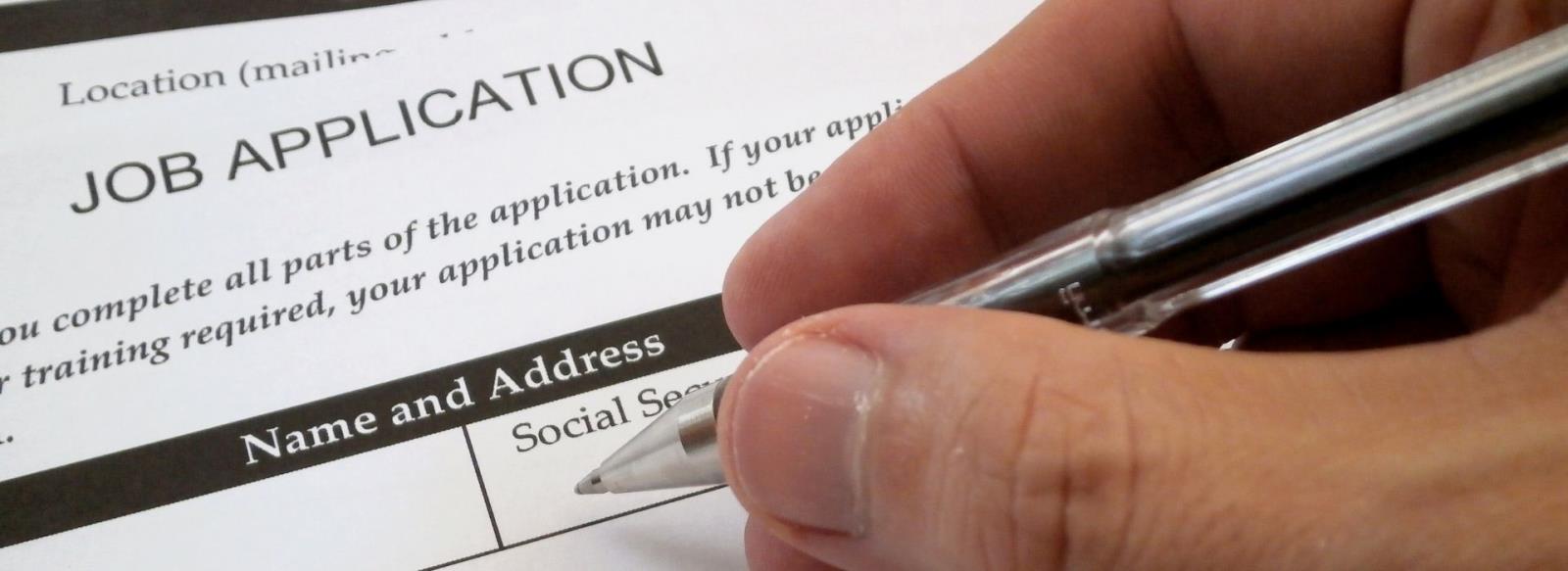 Image of hands holding a pen filling out a job application.